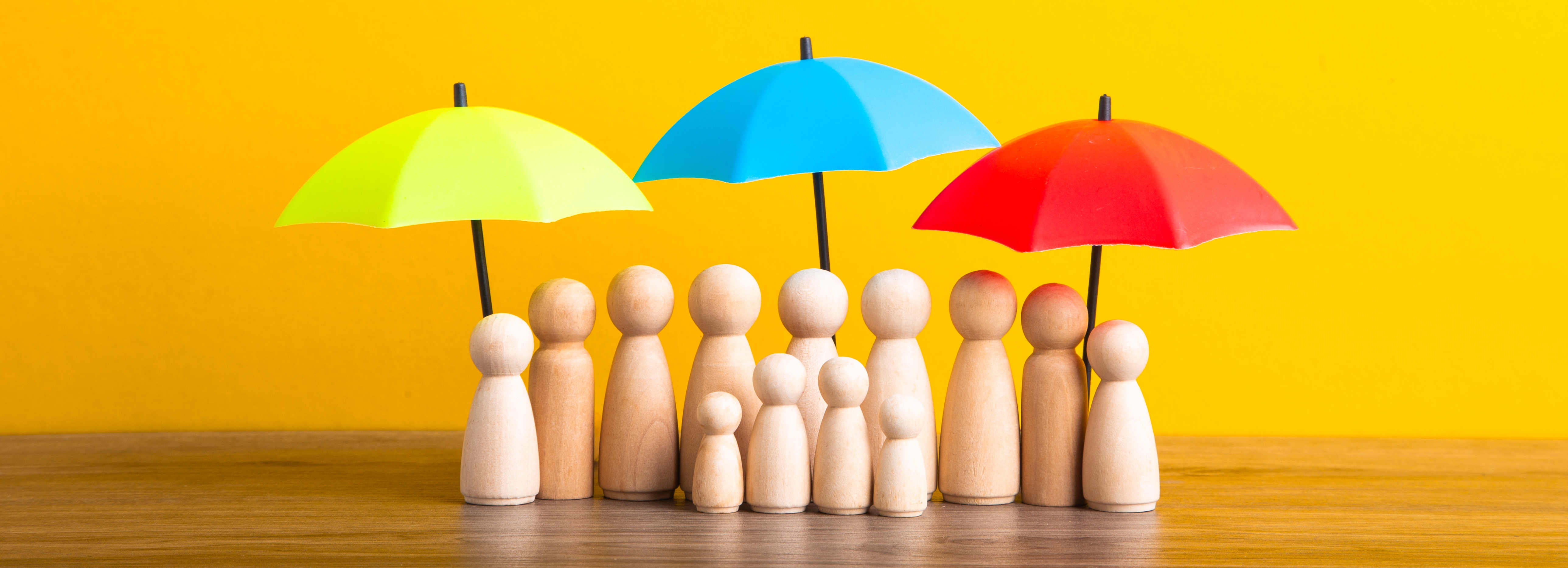 Wooden family figures protected under colorful umbrellas representing comprehensive commercial umbrella insurance coverage for businesses and their stakeholders