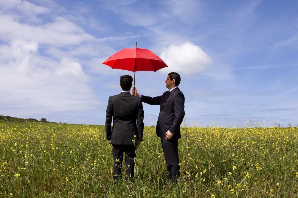 Two businessmen sharing red umbrella in field representing personal umbrella insurance protection and additional coverage