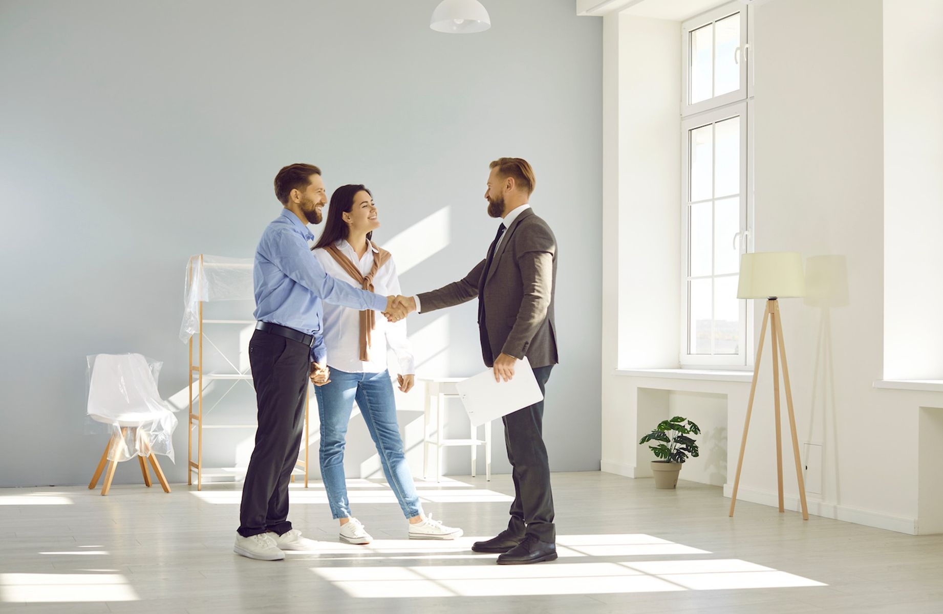Young couple shaking hands with landlord or real estate agent in modern apartment representing renters insurance coverage for tenant agreements