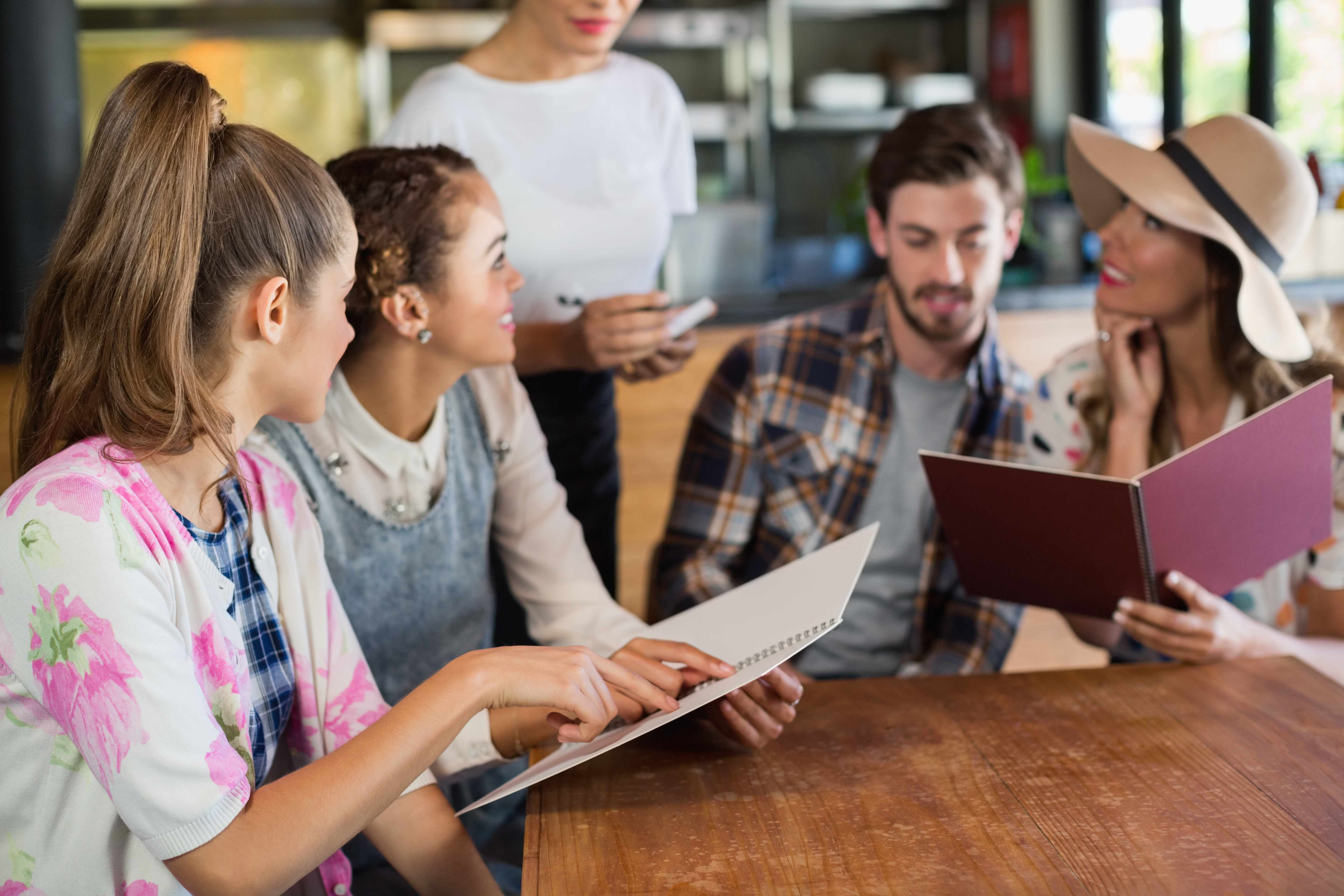 Young customers reviewing menus and discussing their order with restaurant staff representing customer service protection through comprehensive restaurant insurance