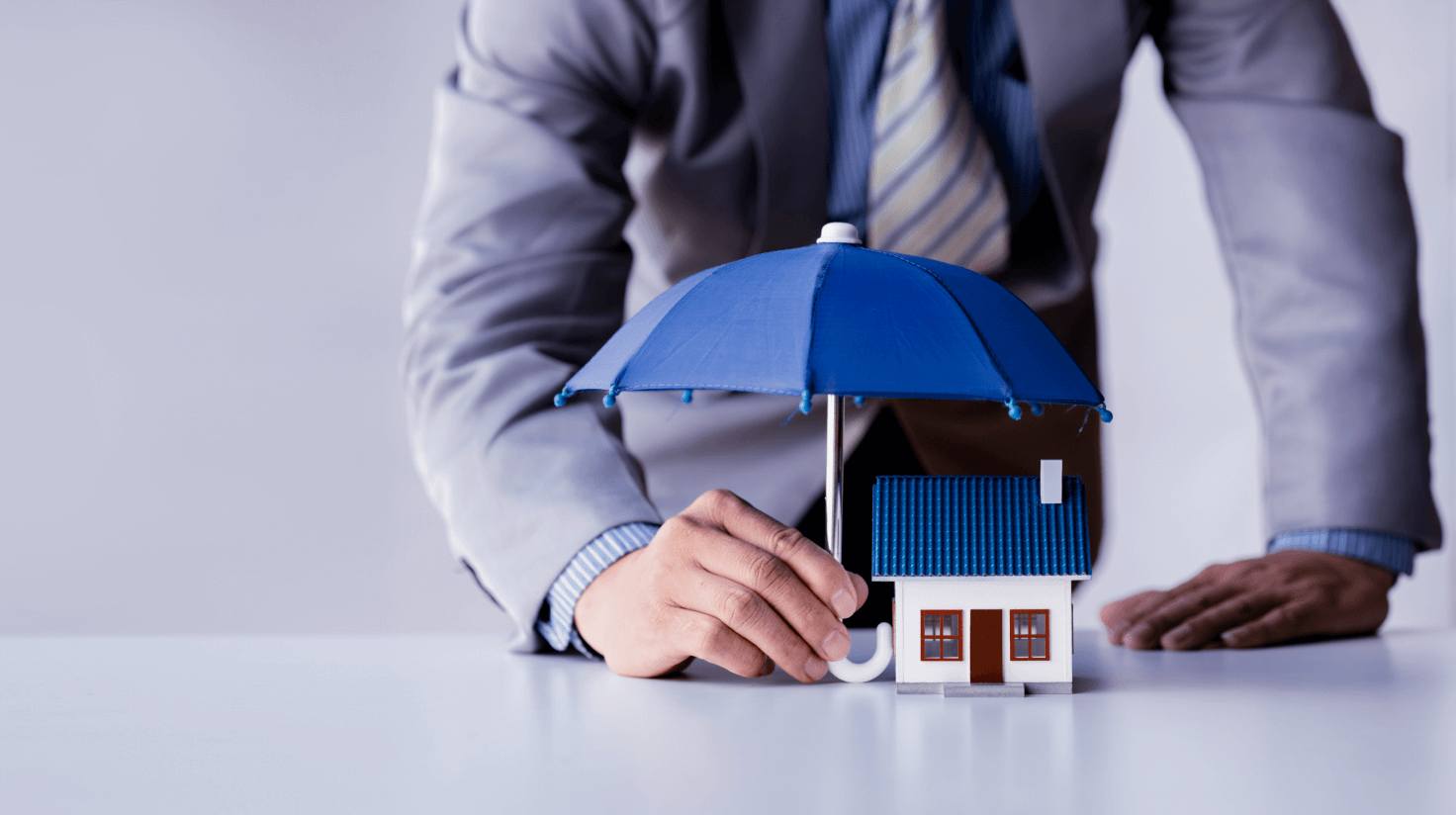 Professional protecting model house with blue umbrella representing personal umbrella insurance coverage